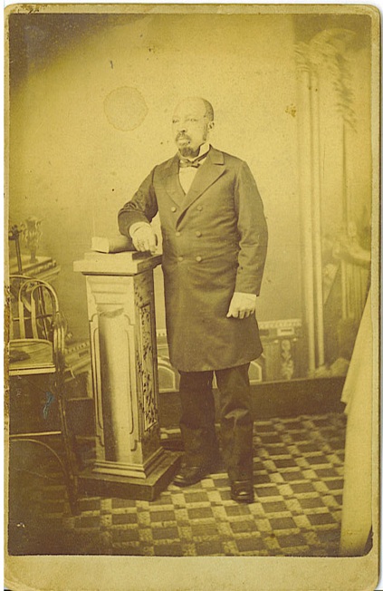 Cabinet card circa 1880s showing a distinguished looking standing African American man, his right arm resting upon a book laying on a pedestal.